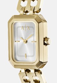 Zlato-tonirana pravokotna ura s srebrnim številčnico, minimalističnimi zlatimi številkami in obliko zapestnice s povezavami. Šesterokotna podrobnost na kroni.