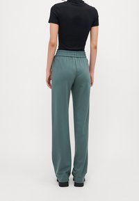 Gröna vida byxor med elastisk midja, tillverkade av mjukt tyg, parat med en svart kortärmad topp. Slät textur och avslappnad passform.