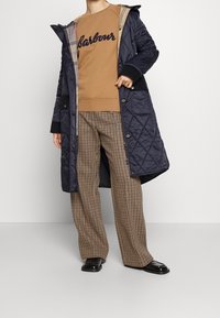 Navy quilted long coat with a hood, black accents, and plaid lining. Brown sweatshirt with "Barbour" text and check-patterned wide-leg trousers.
