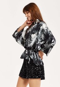 Black and white patterned satin top with wide sleeves, cinched at the waist. Paired with textured black sequin shorts, mid-thigh length.