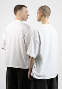 White oversized t-shirts made of cotton, featuring short sleeves and back neck labels. Paired with dark, baggy jeans.