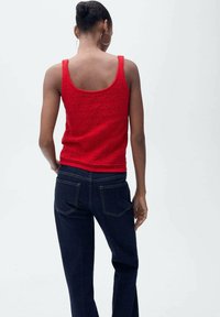 Canotta rossa con un motivo testurizzato, abbinata a jeans blu scuro. La canotta ha uno scollo a v e un design aderente, con orlo semplice.