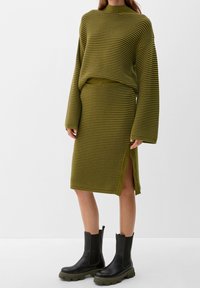 Ensemble deux pièces en maille vert olive à rayures horizontales. Pull oversize à larges manches et texture côtelée, associé à une jupe ajustée avec fente latérale.