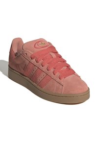 Baskets basses en daim rose avec des lacets épais, trois bandes latérales, semelle beige et logo doré sur la languette.