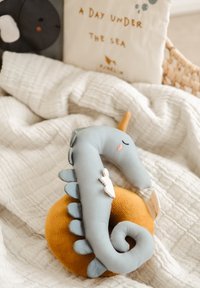 Soft, plush seahorse toy in pastel blue and orange. Features scales, a curled tail, and a stitched face. Set on a textured white blanket.