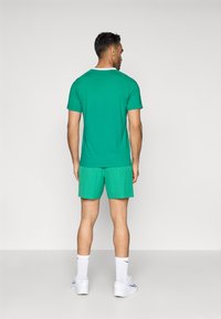 Πράσινο βαμβακερό T-shirt και παντελόνι κοντομάνικο με σχέδιο. Το σύνολο διαθέτει κοντά μανίκια, λαιμόκοψη τύπου crew και υφή, σε συνδυασμό με λευκά αθλητικά παπούτσια.