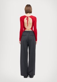 Red ribbed long-sleeve top with open back, tied detail, paired with high-waisted, gray wide-leg trousers. Smooth fabric, structured fit.