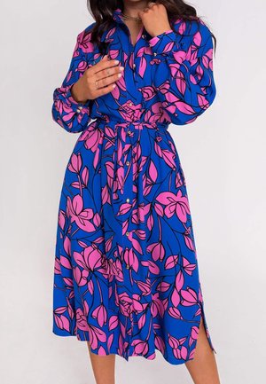 Modré šaty s výrazným růžovým květinovým vzorem, dlouhými rukávy, zapínáním na knoflíky vpředu, páskem v pase a bočními rozparky, vyrobené z lehké látky.
