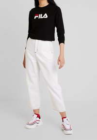 Svart kortärmad långärmad tröja med "FILA"-logotyp, vita högmidjade vida byxor och vita sneakers med röda detaljer.