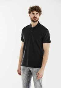 Black polo shirt with short sleeves, three-button placket, plain design, made from smooth fabric, paired with light gray, faded jeans.