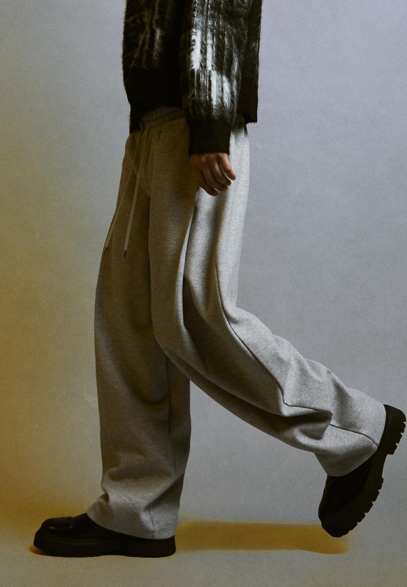 Pantaloni grigi in felpa con una vestibilità ampia, vita elastica e tasche laterali, abbinati a sneakers nere chunky; tessuto testurizzato.