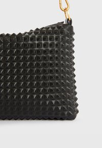 Sort håndtaske lavet af tekstureret materiale med et pyramidemønster, med en lynlåslukning og en guldkædeaccent.