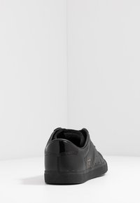 Black leather sneaker with a smooth finish, textured heel, and a rubber sole. Features small ventilation holes and minimal branding.