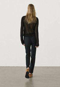 Black knit sweater with open mesh design, paired with fitted black pants and brown platform shoes. Model viewed from the back.