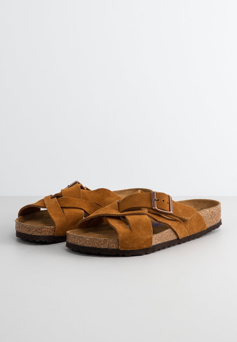 Sandales en daim marron avec des lanières croisées, boucle ajustable et semelle intérieure en liège. Semelle extérieure en caoutchouc avec une adhérence texturée.