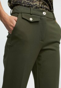Pantalones ajustados verde oliva con una textura suave, que cuentan con un bolsillo delantero con solapa y cierre de botón, y un diseño clásico de pierna recta.