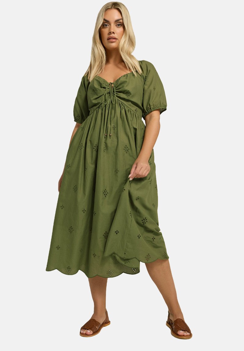 Oliivinvihreä puuvillalDressi, jossa on puffihihat, solmittava etuosa ja aallotettu helma. Sisältää kukkakuvioisia brodeerauksia ja löysän, lentävän leikkauksen.