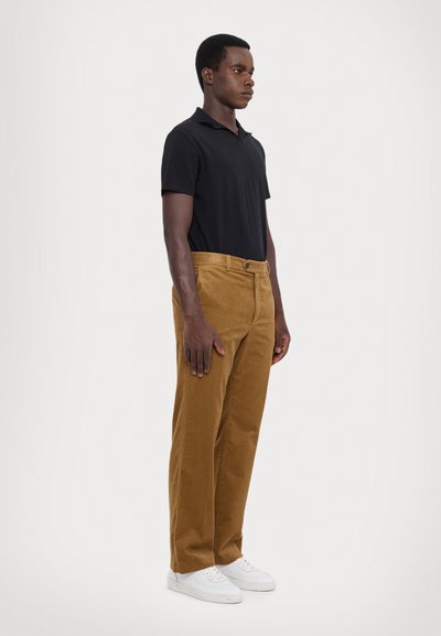 Polo noir, pantalon en velours côtelé marron et baskets blanches. Les pantalons sont dotés de poches latérales et d'une fermeture à bouton. Texture lisse.