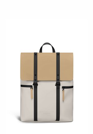 Zaino beige e crema con cinghie verticali nere, due tasche frontali con cerniera e una maniglia superiore, marchiato Gaston Luga Stockholm.