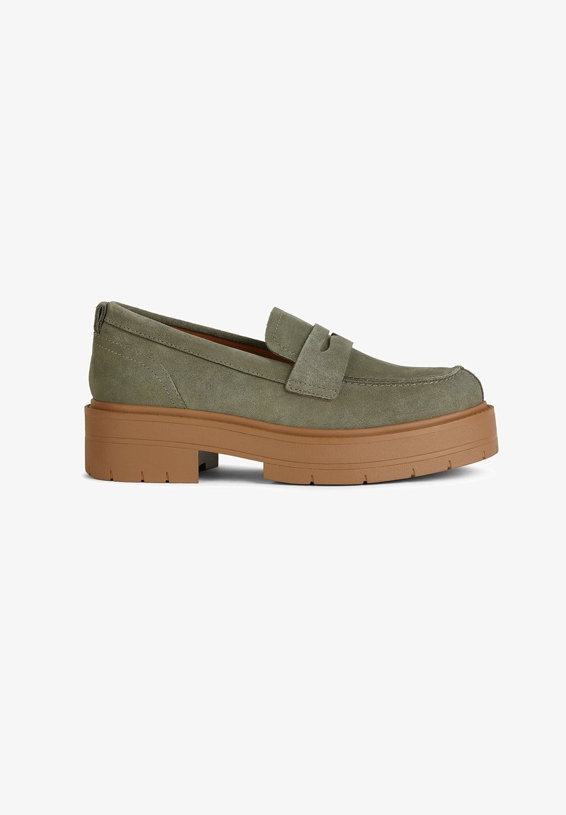 Mocassin en daim vert olive avec un bout arrondi, une semelle plateforme épaisse couleur tan et une couture décorative sur le dessus. Comprend une lanière ornementale traversant le coup de pied.