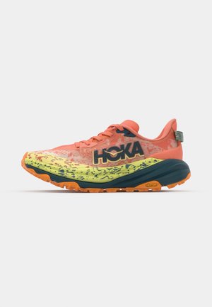 Hoka running shoe featuring a bright orange upper with a yellow and green patterned sole. Lightweight design with textured detailing and Vibram logo.