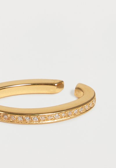 Χρυσό βραχιόλι με ανοιχτό μανσέτα και σειρά μικρών διαφανών κρυστάλλων τοποθετημένων κατά μήκος της εξωτερικής άκρης σε λευκό φόντο.