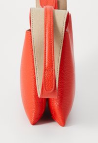 Sac à main en cuir bicolore orange et beige avec une large poignée supérieure, présenté de côté sur fond blanc.