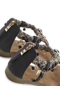 Schwarze Sandalen mit geflochtenen Leopardenmuster-Riemen, goldfarbigen Hardware-Details, Reißverschlüssen und dekorativen Ketten mit Perlen auf einer beigefarbenen gepolsterten Sohle.