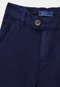 Marineblaue Hosen mit glatter Textur, elastischem Bund und Knopfverschluss. Sie verfügen über ein kleines Markenetikett und seitliche Taschen.