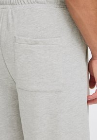 Jasnoszare dresy wykonane z teksturowanego materiału, z elastycznym pasem i kieszenią naszywaną po prawej stronie.