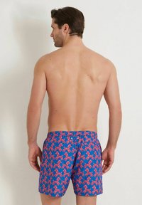 Shorts de bain bleus avec un motif répétitif d'animaux en ballon roses, taille élastique et fermeture par un bouton à l'arrière.