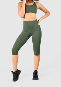 Reggiseno sportivo verde oliva e leggings capri a vita alta realizzati in tessuto morbido, abbinati a scarpe da ginnastica nere.