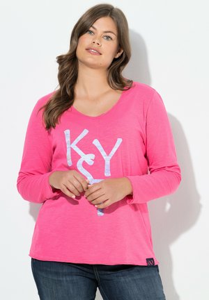 Maglietta a maniche lunghe con scollo a V di un brillante rosa con testo grafico bianco. Tessuto morbido, vestibilità rilassata e orlo curvo. Abbinata a jeans blu scuro.