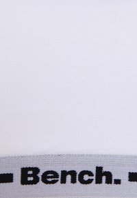 Weißer Baumwollstoff mit gerippter Textur, versehen mit einem grauen elastischen Bund, auf dem "Bench." in fetten schwarzen Buchstaben gedruckt ist.