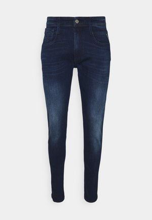 Jean slim bleu foncé avec fermeture par boutons, poches avant et arrière, et détails subtils délavés sur les cuisses et les genoux.