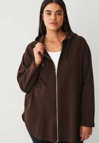 Brown zip-up hoodie with a smooth texture, adjustable drawstrings, and silver zipper. Features a relaxed fit and raglan sleeves.