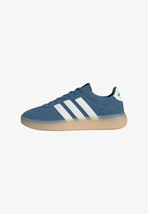 Blue suede sneaker with white stripes. Features a rounded toe and translucent beige outsole. Lace-up design with padded collar.