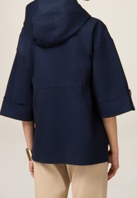 Veste à capuche bleu marine à manches courtes, avec des poignets retroussés et une coupe décontractée. Confectionnée dans un tissu lisse et léger. Design simple.