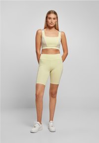 Svijetlo žuti sportski crop top i biciklističke kratke hlače, elegantnog dizajna s kvadratnim dekolteom, s pastelnoplavim naglascima na naramenicama, glatke teksture.