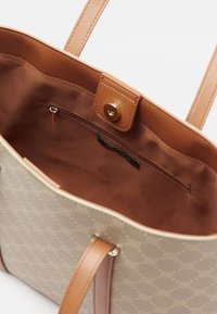 Sac fourre-tout beige avec accents en cuir brun clair et poignées ; intérieur doté d'une poche zippée et d'une doublure en tissu doux. Extérieur à motif.