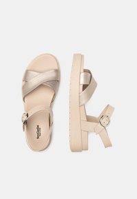 Beige sandals featuring crossed metallic straps and a buckle closure on the ankle. The sole is thick with a textured design for grip.