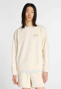 Lichtbeige sweatshirt met lange mouwen, ribgebreide manchetten en een ronde hals. Heeft een klein bedrukt logo op de borst en een relaxte pasvorm.