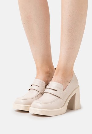 Chaussures à talons blocs en cuir beige avec un bout arrondi, dotées de doubles accents de bride et d'une semelle texturée. Fini lisse avec des lignes épurées.