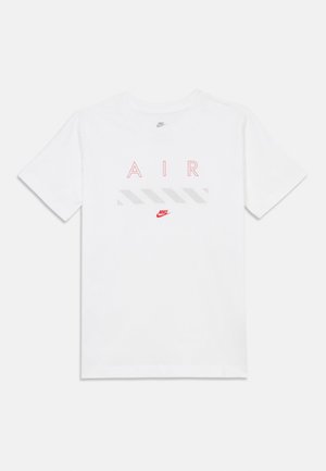 La camiseta blanca de manga corta presenta "AIR" en letras rojas sobre una franja gris, con un pequeño logo rojo de Nike en la parte inferior central.