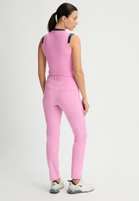Pink sleeveless top and matching slim-fit pants, both made from smooth fabric. Top features navy shoulder accents; outfit paired with white sneakers.