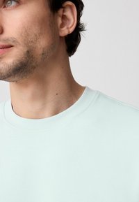 Svjetlo mint zelena dukserica s okruglim izrezom, nježne teksture, s jednostavnim dizajnom i suptilnim detaljima šivanja oko ovratnika.
