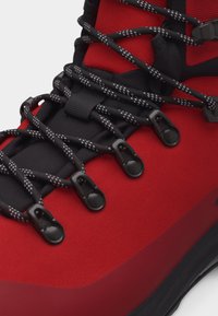 Czerwony but turystyczny z czarnymi i szarymi odblaskowymi sznurówkami przeplatanymi przez metalowe haczyki na czarnym, wyściełanym języku.