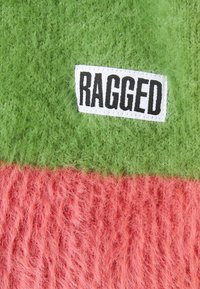 Fuzzy, plush fabric in green and pink sections, featuring a stitched "RAGGED" label. The texture is soft with a shaggy appearance.