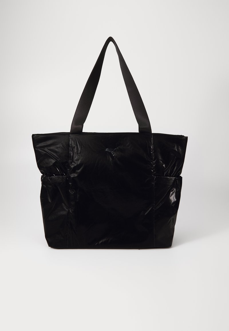 Μαύρη τσάντα tote από γυαλιστερό υλικό, σε ορθογώνιο σχήμα, με δύο επάνω λαβές και δύο πλαϊνές τσέπες. Απλό σχέδιο με ελάχιστες διακοσμήσεις.