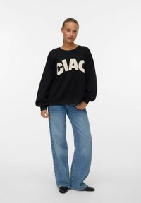 Zwarte oversized sweatshirt met crèmekleurig "CIAC" logo, ronde halslijn en lange pofmouwen. Gecombineerd met lichtblauwe wijde jeans.